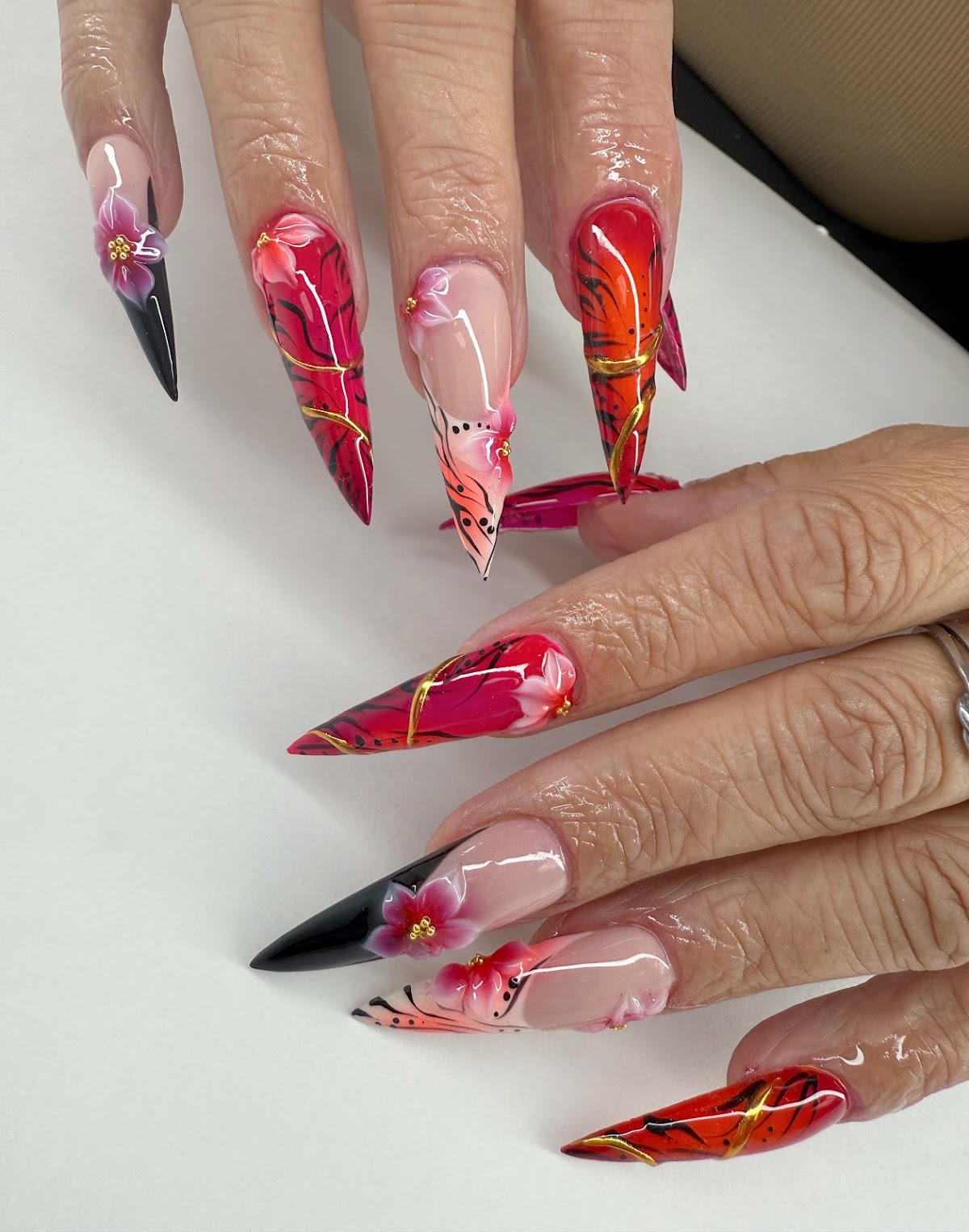 Long stiletto nails with red and fuchsia florals, gold linework and black detail